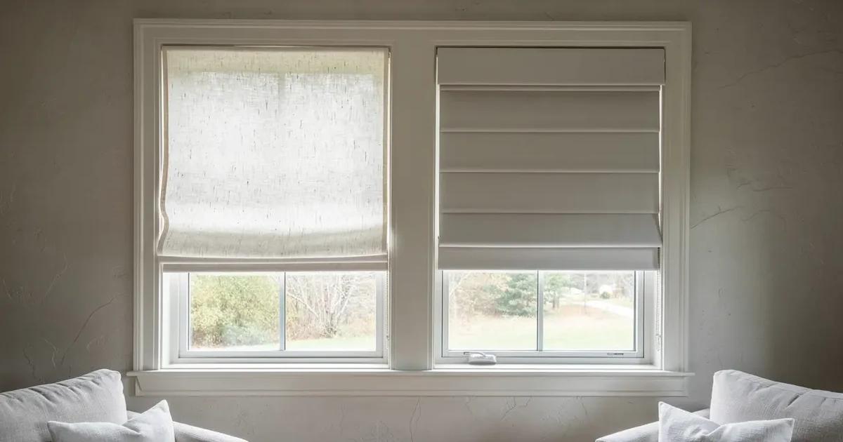 Deux stores romains sur mesure dans un salon de l'Estrie, l'un en lin lavé au pli souple et arrondi, l'autre en coton ferme au pli plat et taillé, lumière du matin traversant les deux, mur de plâtre pâle