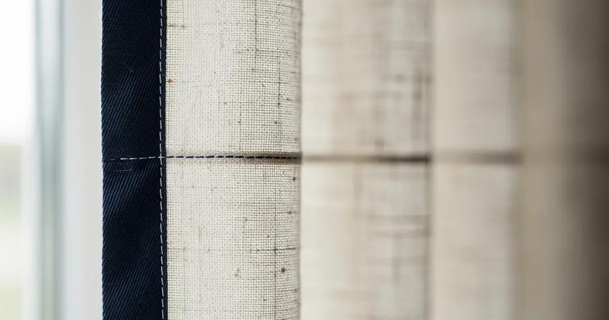 Détail du bord menant d'un rideau en lin écru orné d'une bande contrastante en coton bleu marine large de huit centimètres, couture nette visible de près, plis réguliers, lumière naturelle latérale dans un atelier de Sherbrooke