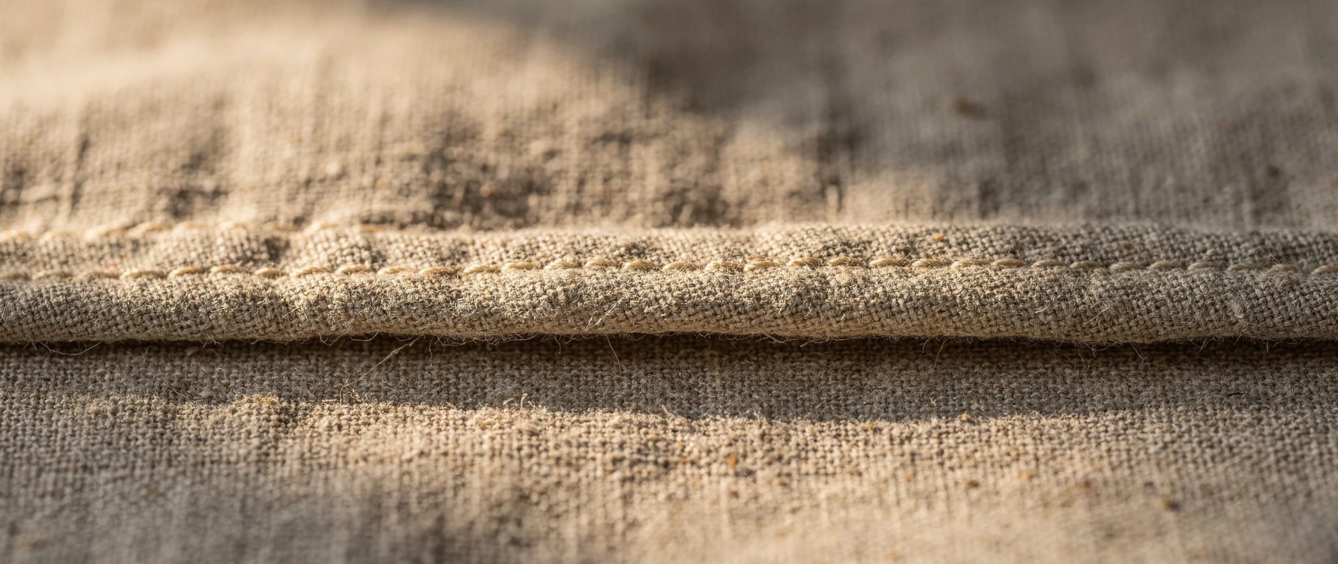 Close-up of a double-turned hem on heavy natural linen, finished with small even stitches in oatmeal thread.