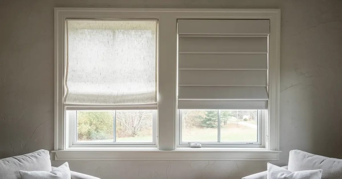 Deux stores romains sur mesure dans un salon de l'Estrie, l'un en lin lavé au pli souple et arrondi, l'autre en coton ferme au pli plat et taillé, lumière du matin traversant les deux, mur de plâtre pâle