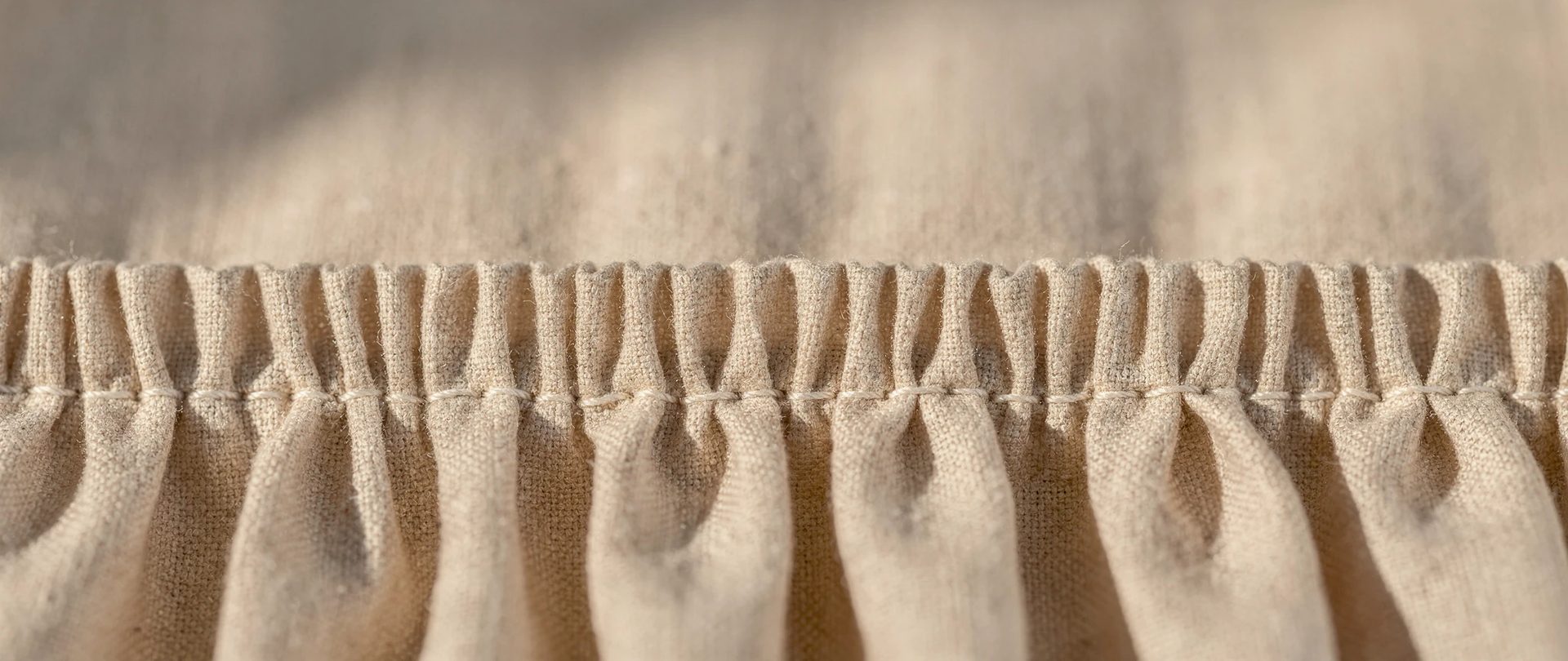 A row of tight gathered pleats stitched along an ecru linen heading tape.