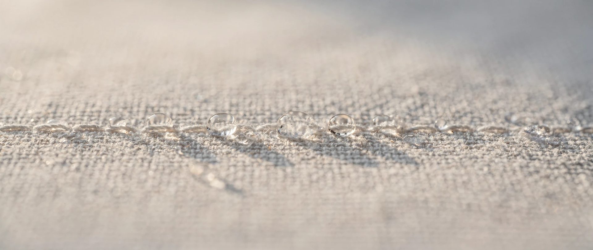 Beads of water sitting on the tight weave of an off-white cotton canvas.