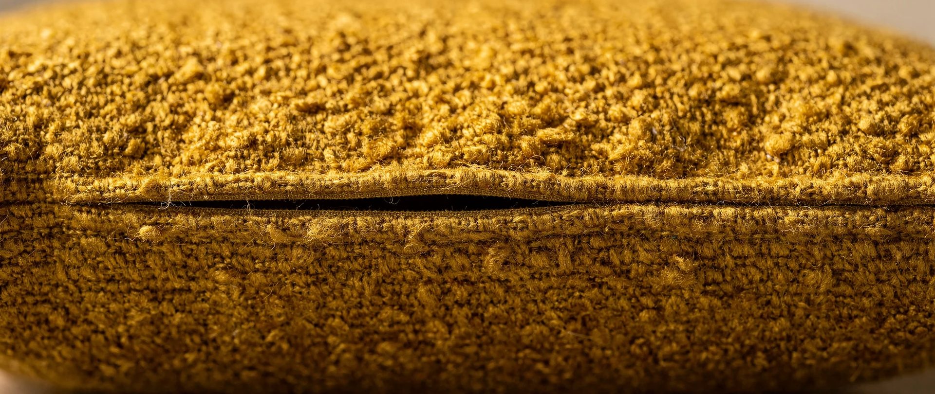 Seam of a mustard bouclé cushion cover with its zipper slightly open.