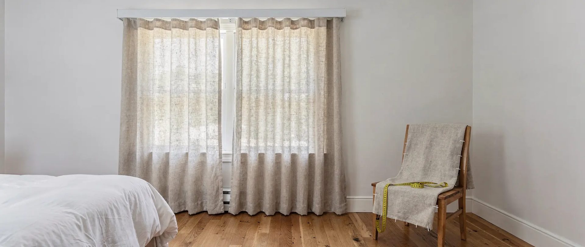 Curtain alterations: linen curtains in a bedroom, with a linen panel pinned to a wooden chair and a yellow tape measure.