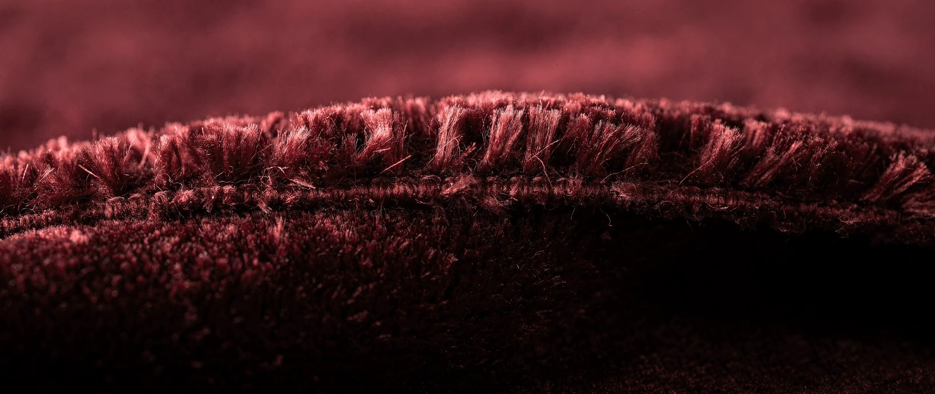 Burgundy velvet with dense pile standing along a ridge above a stitched edge.