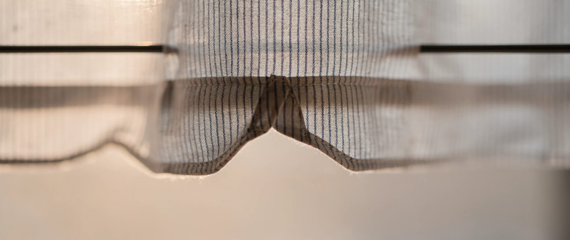Scalloped edge of a pinstriped cotton café curtain threaded on a thin black rod.