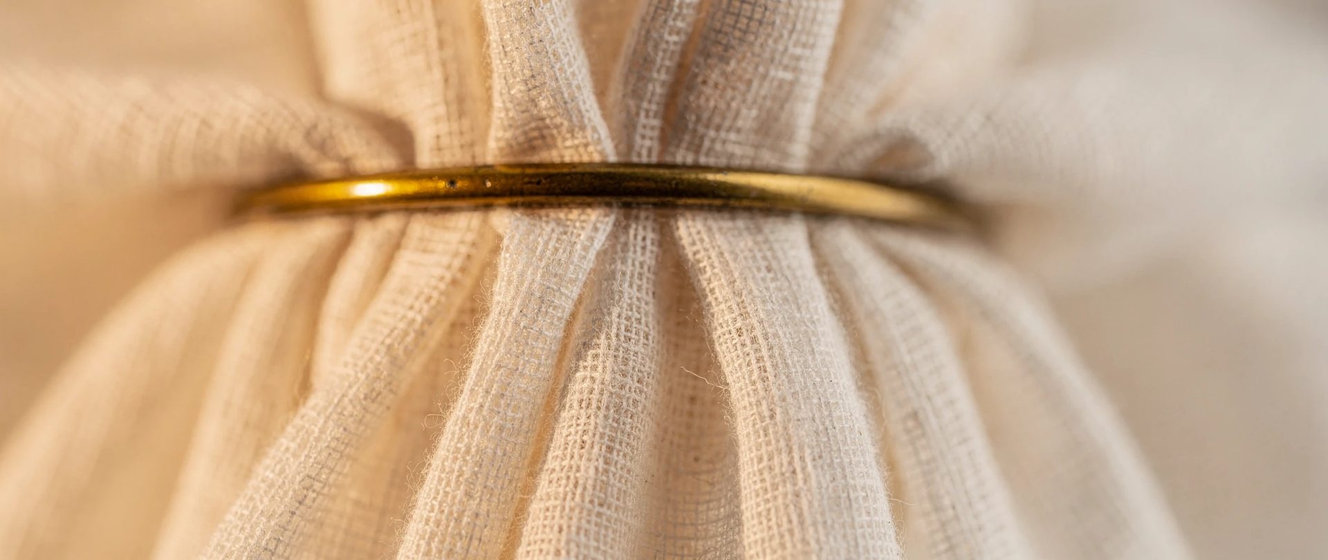 Ivory cotton gauze gathered through a brass ring, with soft pleats falling below.