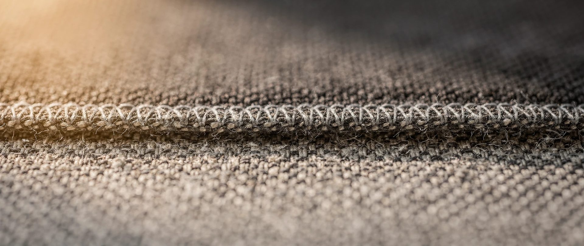 Tissu gris au tissage serré avec un bord surfilé en fil clair, vu de près.