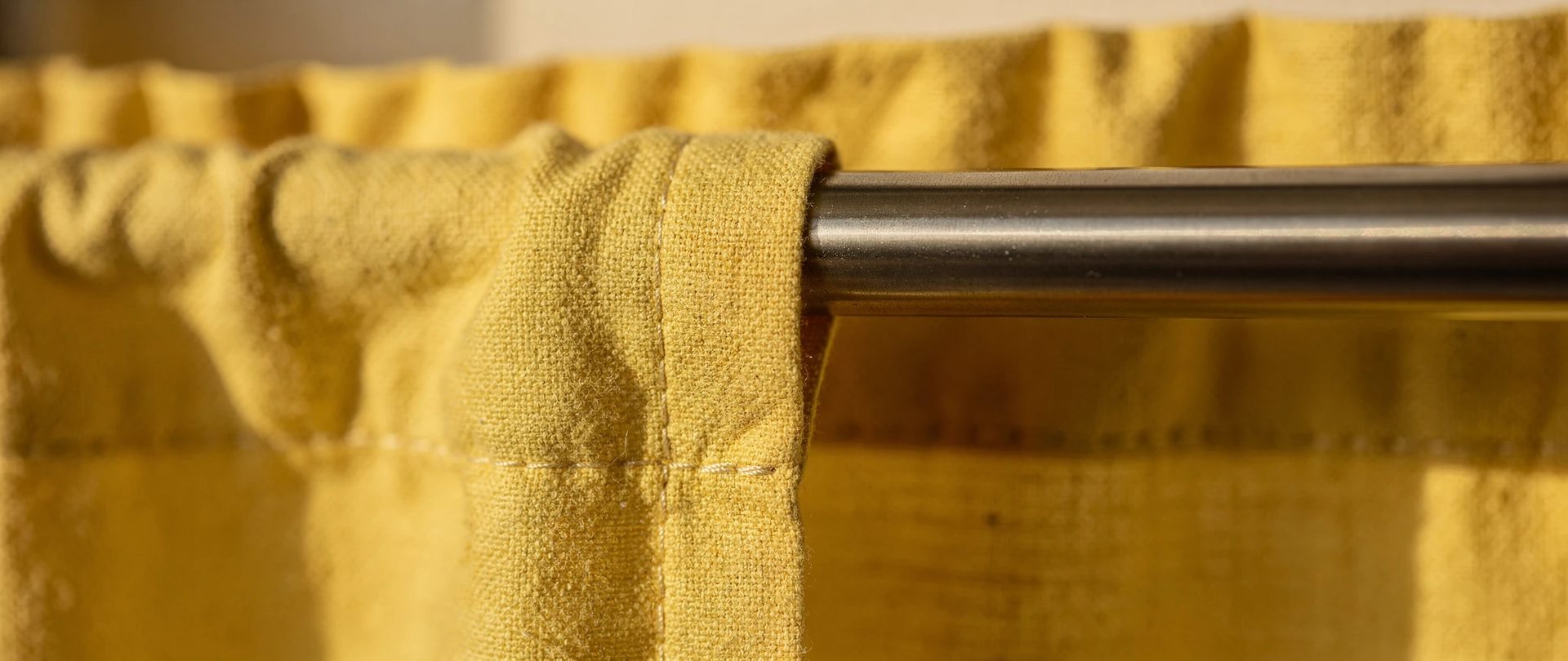 Rod pocket of a short lemon-yellow cotton curtain with a steel rod passing through.