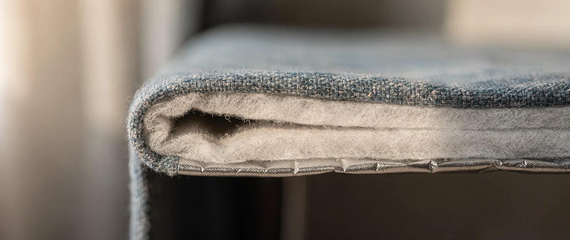 Cut corner of a thermal curtain showing a blue face, white fleece and silvery backing in layers.