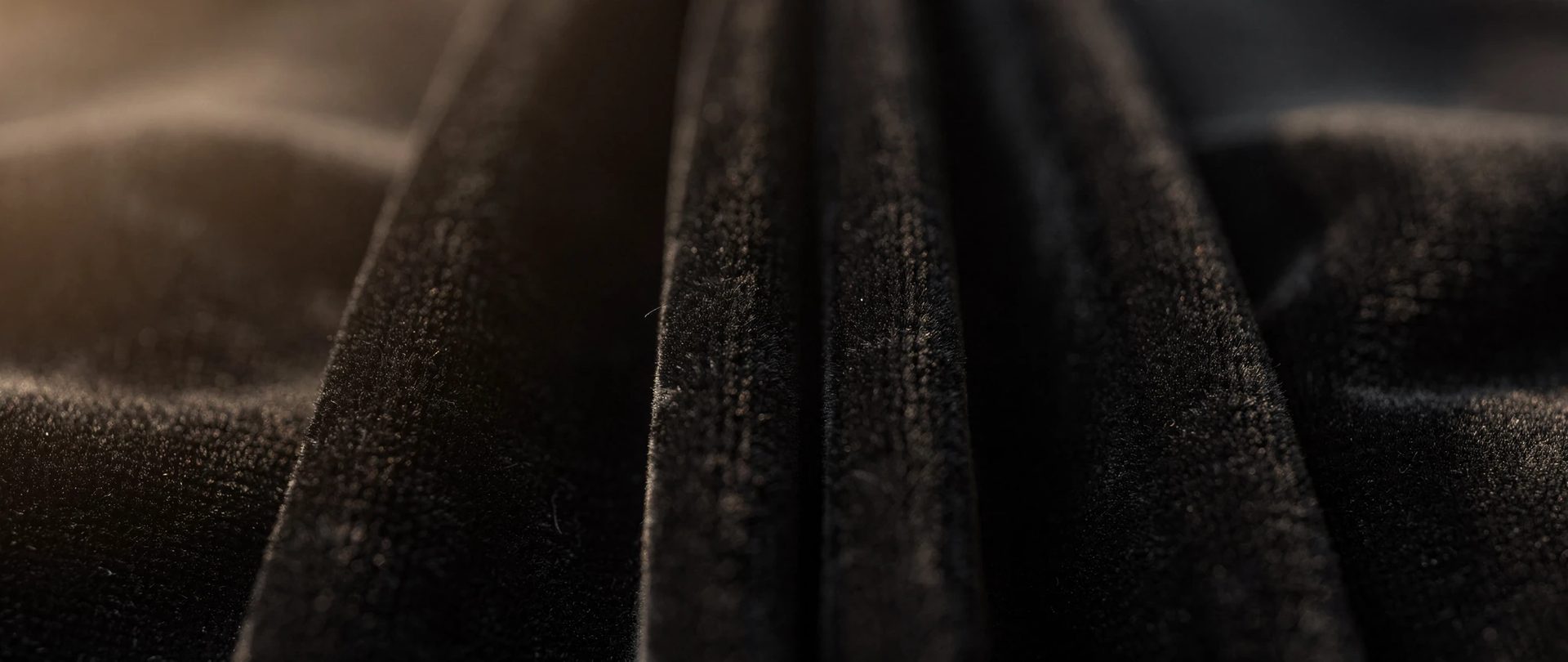Matte black velvet in deep, regular pleats, the pile soaking up the light.