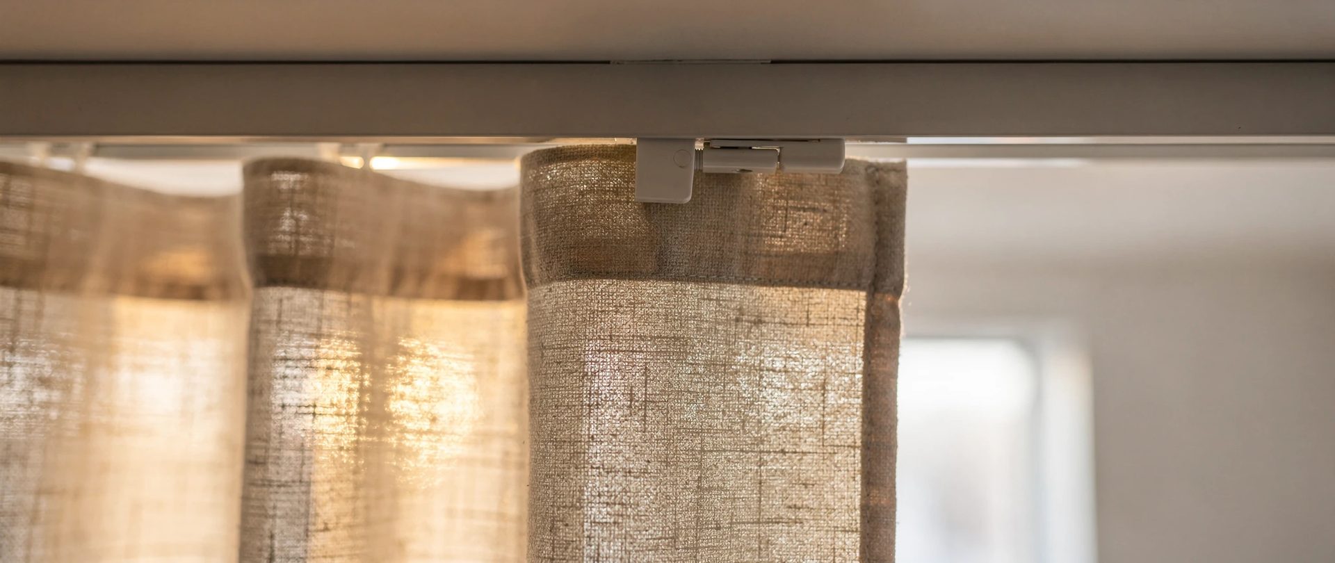 Rail de plafond blanc avec un glisseur qui retient un panneau de lin sable.