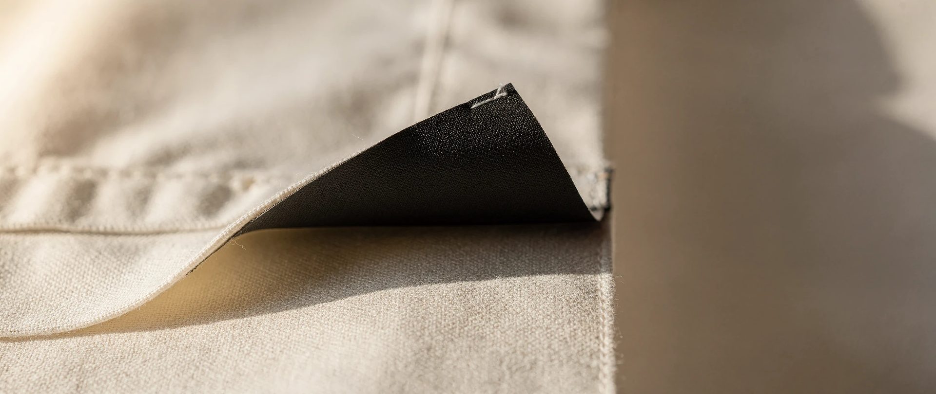 Back of a curtain where the black blackout coating peels away from the cream face fabric.