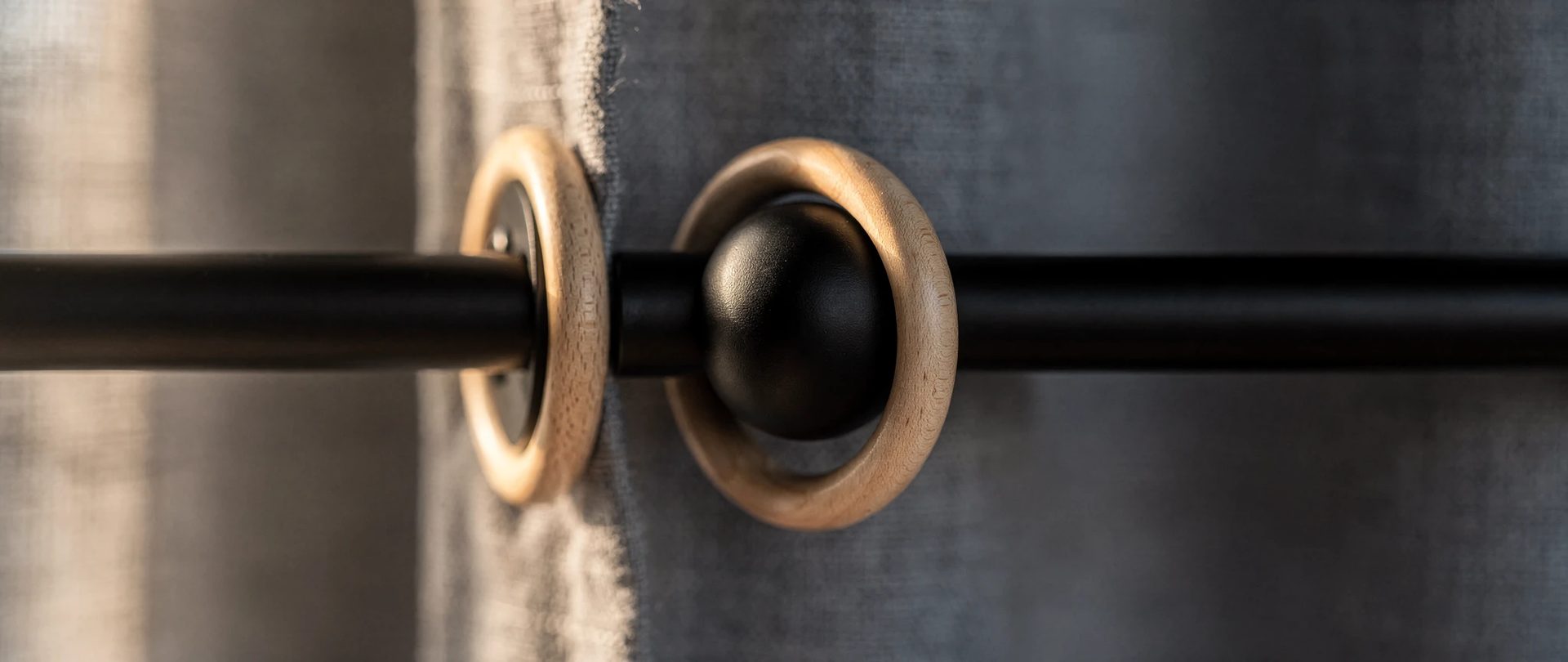 Matte black iron rod with a ball finial and wooden rings against slate-grey fabric.