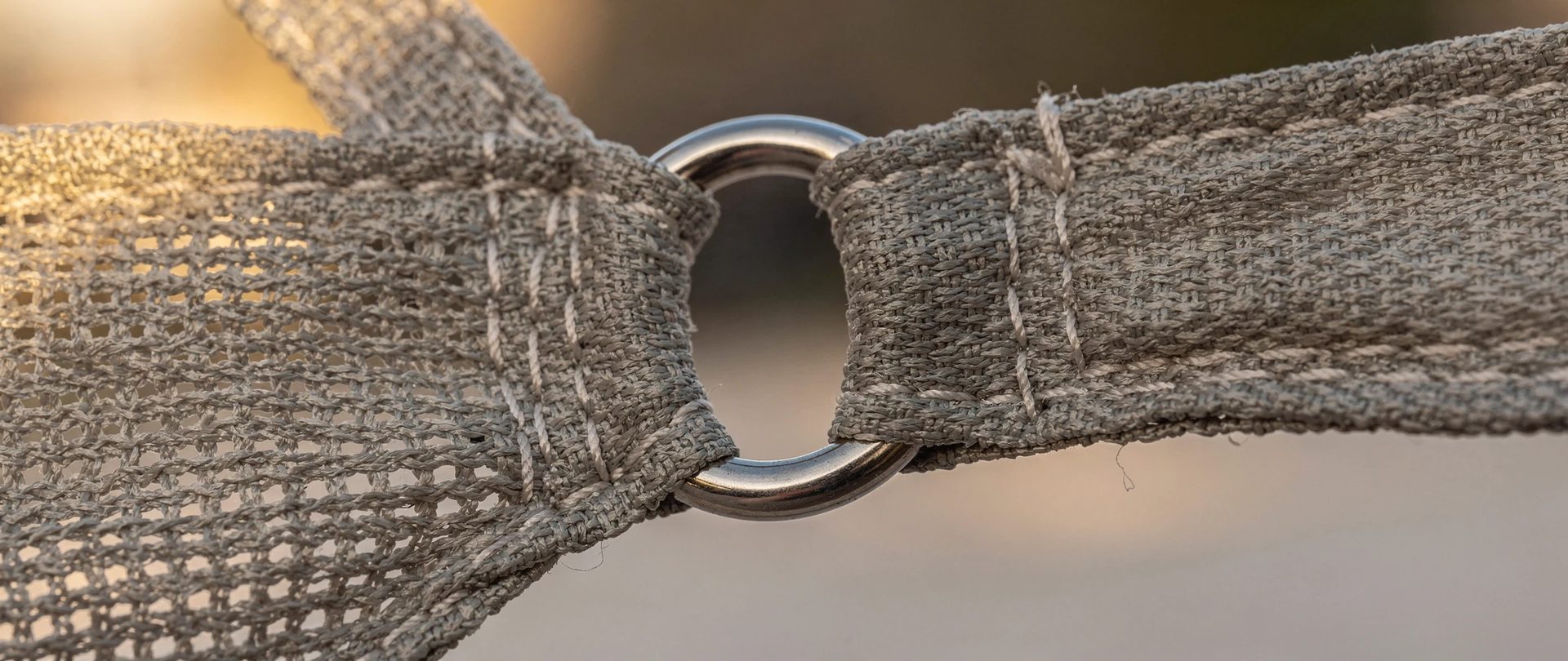 Corner of a grey knitted shade sail with stitched webbing and a stainless steel ring.